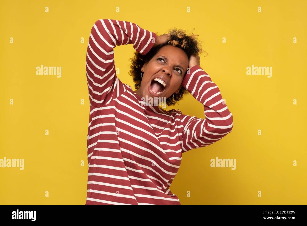 Junge wütende afrikanische Frau irritiert und mit dummen Worten. Studio auf gelber Wand. Stockfoto
