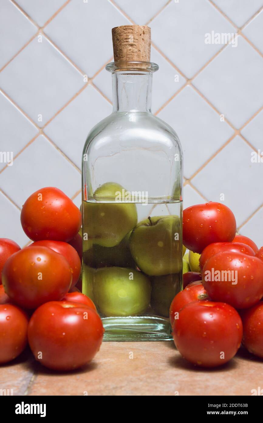 Nahaufnahme von Äpfeln durch die Wirkung von Wasser verzerrt. Dreieckige Zusammensetzung aus Äpfeln, Tomaten und einer Flasche Glas auf der Küchentheke. Stockfoto