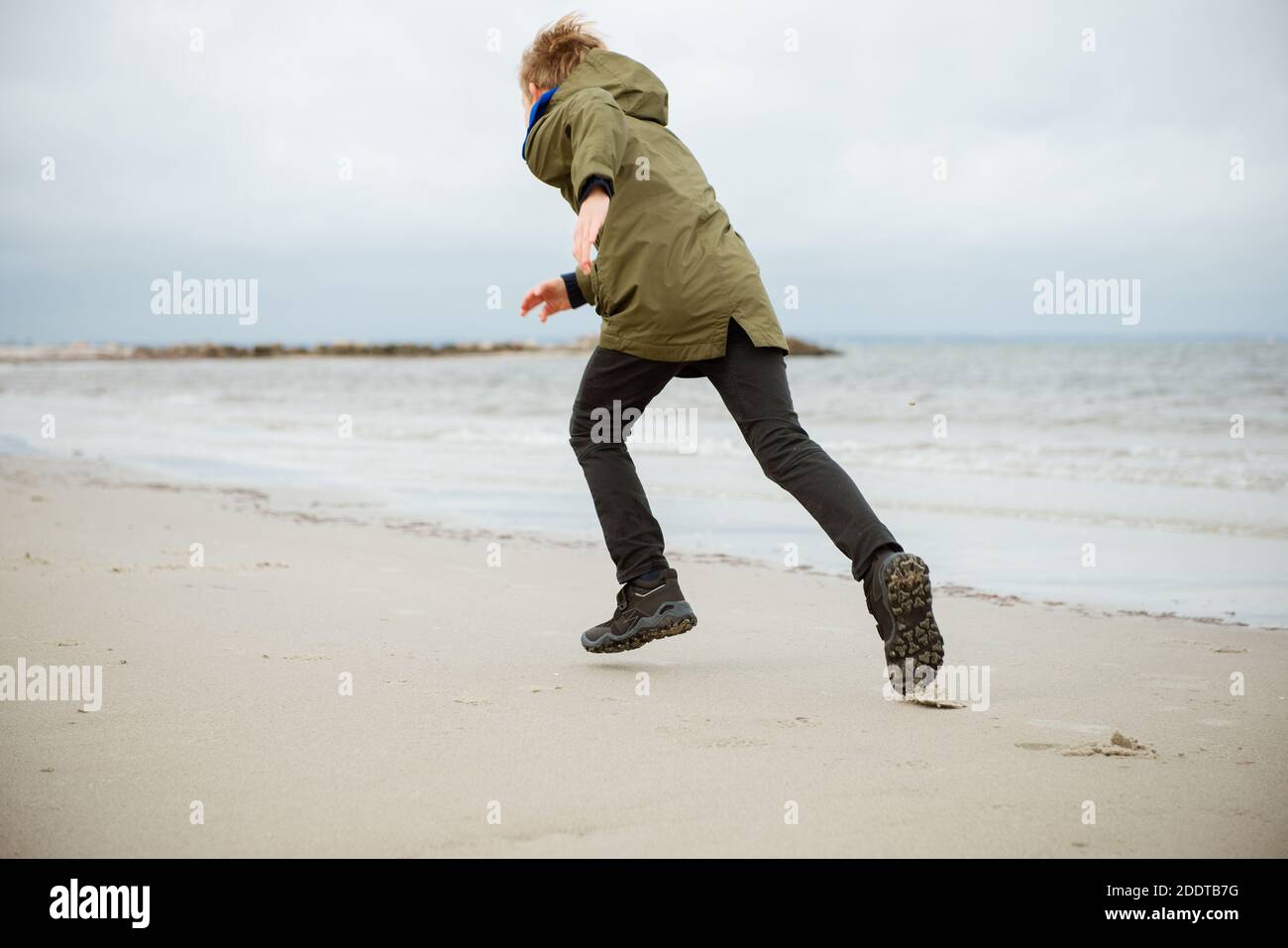 Glücklicher Teenager Junge läuft auf dem Wasser der Ostsee in Gummistiefel  bei kaltem und windigem Wetter Stockfotografie - Alamy