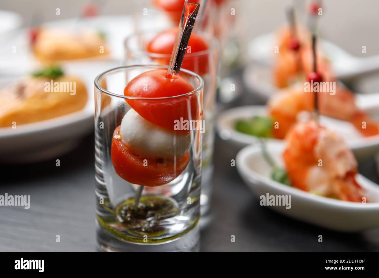 Kirschtomaten und Mozzarella Canapes auf Spieße in einem Glas Glas mit einem Hintergrund von Garnelen in Nahaufnahme Stockfoto