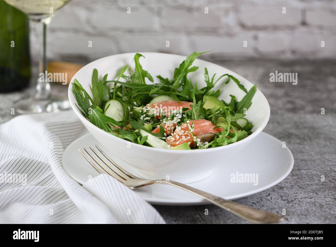 Gemüsesalat aus Rucola, Avocado und Gurkenstücken mit Zusatz von zartem gesalzenem Lachs, gewürzten Sesamkörnern Stockfoto