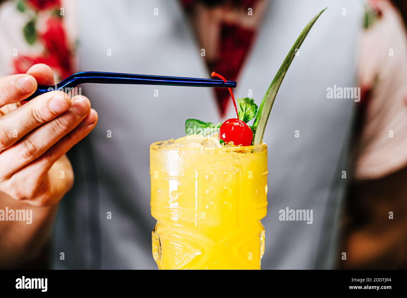 Der Barkeeper bringt eine Kirsche auf einen Tiki-Cocktail Stockfoto