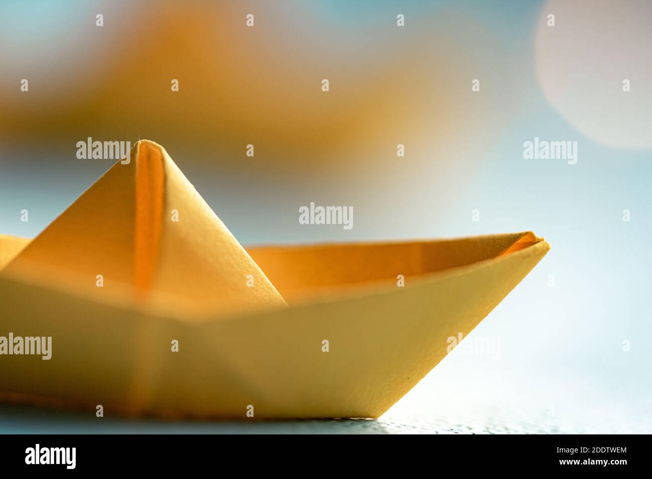 Origami gelbes Segelboot auf einem Meer mit blauem Papier. Hintergrund im Papierkunststil mit Schiffen, Ozeanen und Bokeh-Lichtern Stockfoto