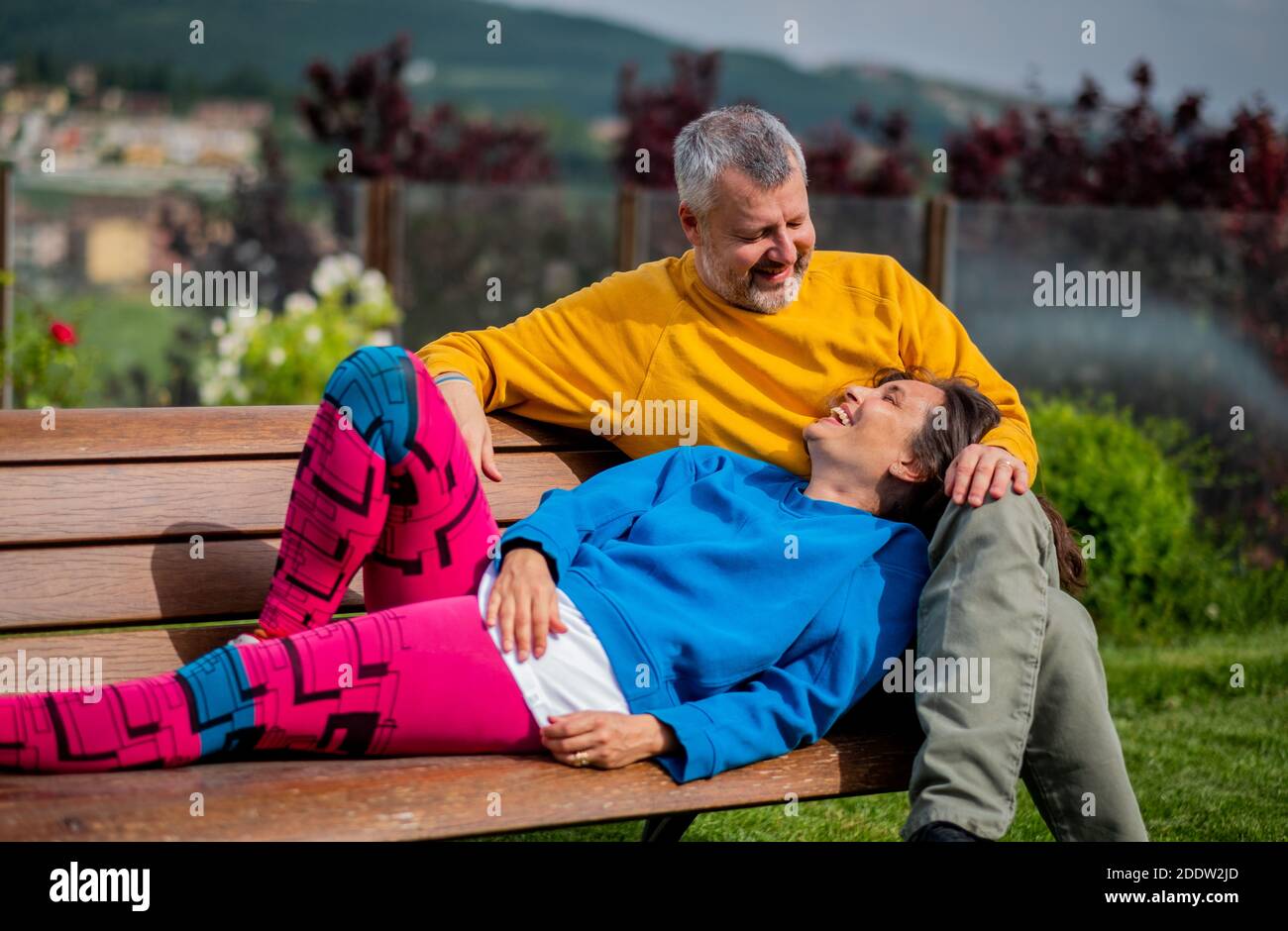 Attraktives Ehepaar im Park entspannen - glückliche Liebhaber Und sportliches Paar auf der Bank - Paar sitzt auf Außenbank zusammen Stockfoto