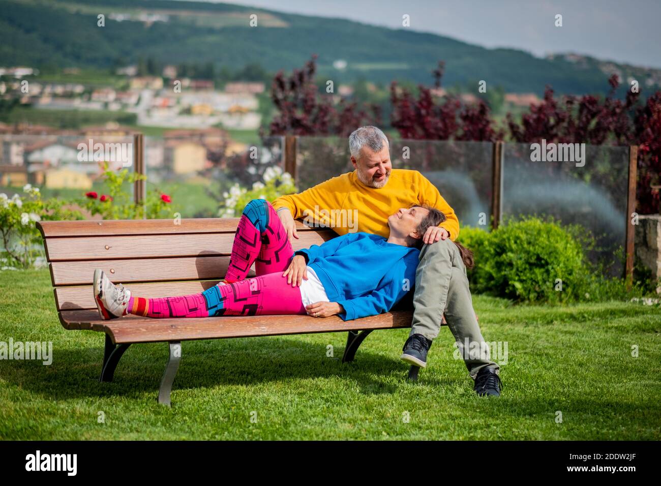 Attraktives Ehepaar im Park entspannen - glückliche Liebhaber Und sportliches Paar auf der Bank - Paar sitzt auf Außenbank zusammen Stockfoto