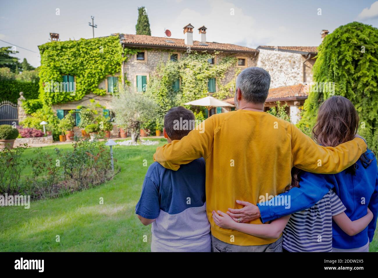 Rückansicht der glücklichen Familie Umarmung steht vor ihrem neuen Haus - Dieses Foto kann für Familie, Vater, Mutter und Hauskonzept Stockfoto