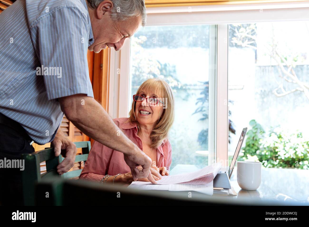 Eine ältere Frau und ein Mann lächeln und reden über Geschäfte. Die Frau ist ein Tisch mit einem Laptop vor ihr. Klares, helles Bild. Stockfoto