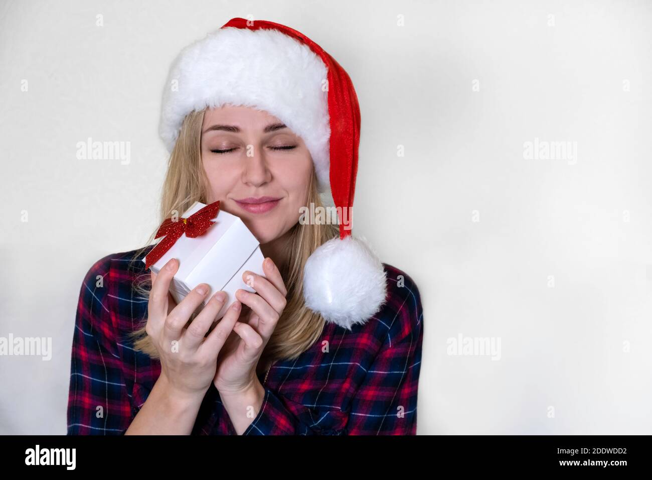 Weihnachtsgeschenk. Junge kaukasische Frau mit Geschenk in ihren Händen lächelt und genießt es, ihre Augen vor einem weißen Hintergrund zu schließen Stockfoto