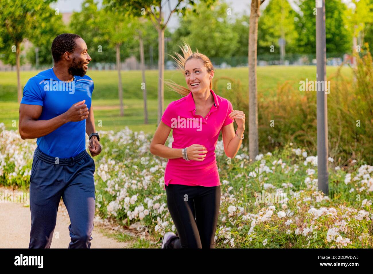 Das junge Paar joggt im Park, um gemeinsam zu laufen. Afro amerikanischer Mann und schöne blonde Mädchen in Sportbekleidung läuft durch den Stadtpark toget Stockfoto