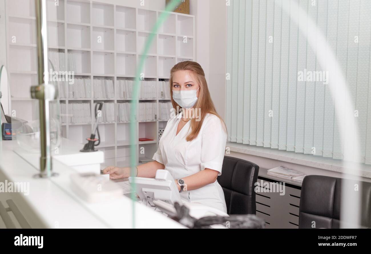 Mädchen-Verwalterin im weißen Mantel und der Maske des Arztes Klinik.Empfang von Patienten.Aufnahme in das Krankenhaus Stockfoto