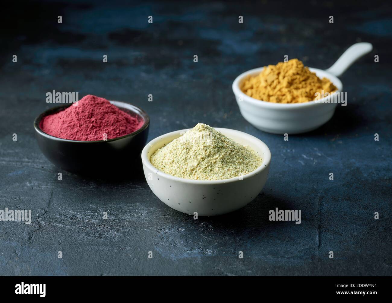 Drei Schüsseln getrocknetes Pflanzenpulver auf tiefblau bemalt Hintergrund Stockfoto