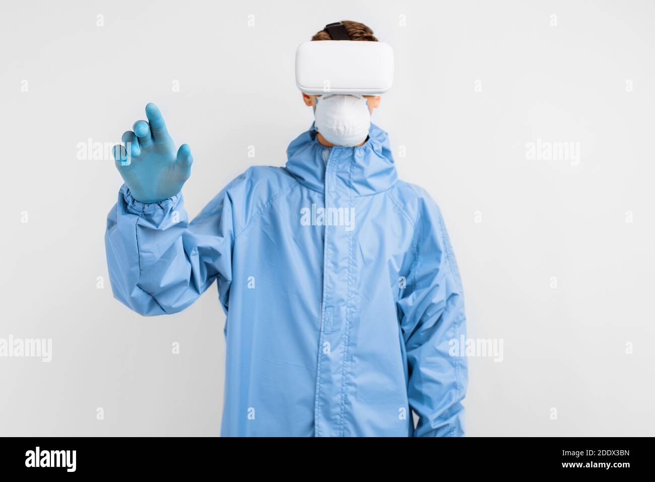 Arzt im Schutzanzug und einer medizinischen Schutzmaske, in einer Virtual-Reality-Brille, auf weißem Hintergrund Stockfoto