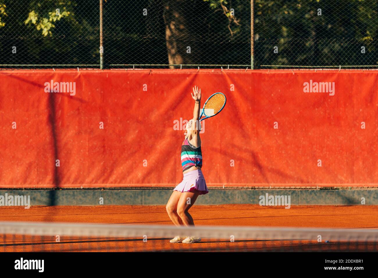 Eine junge, fit Frau spielt Tennis im Freien auf einer Orange Tennisplatz früh am Morgen Stockfoto