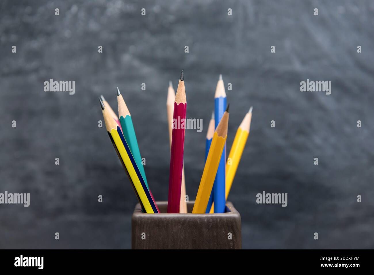 Verschiedene bunte Bleistifte stehen in Halter auf verschwommenem Kreidetafel Hintergrund Stockfoto