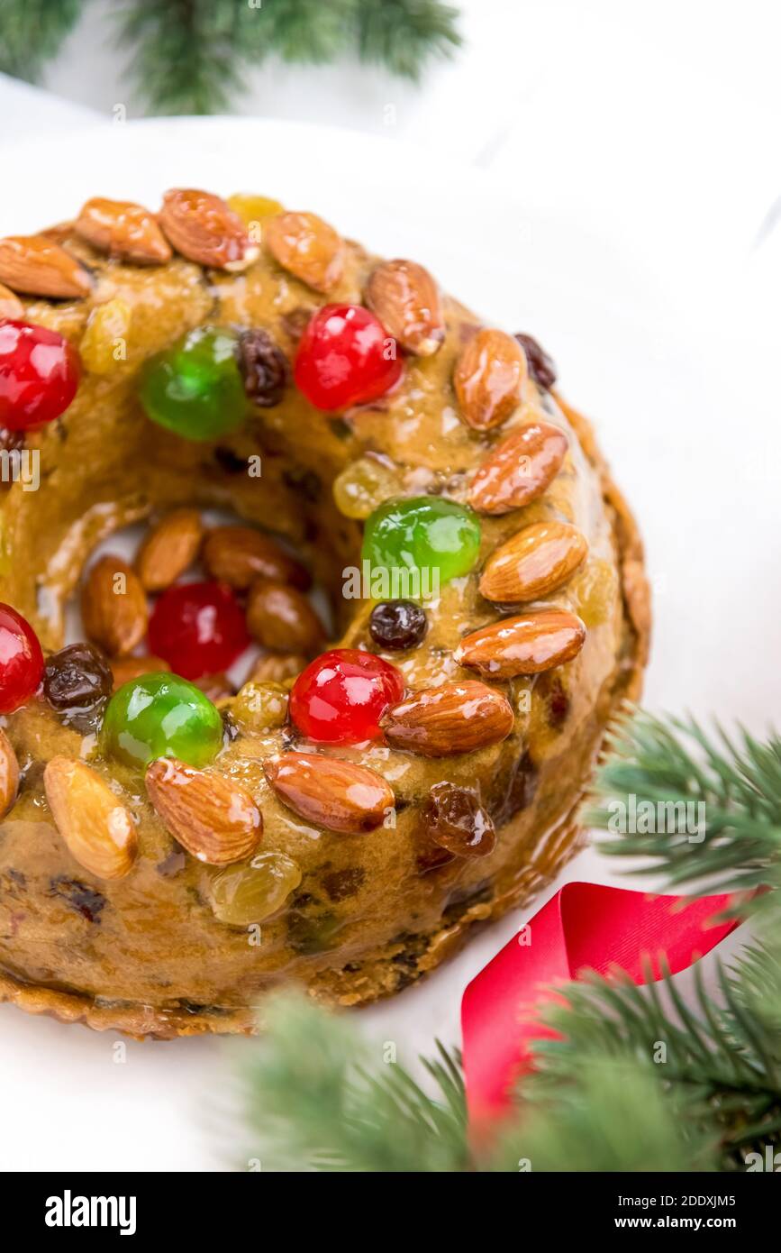 Glasierte runde hohle bunte Weihnachten Obstkuchen gekrönt mit Mandeln und glace Kirschen auf weißem Teller mit grünen Kiefernnadeln und Rote Schleife decorati Stockfoto