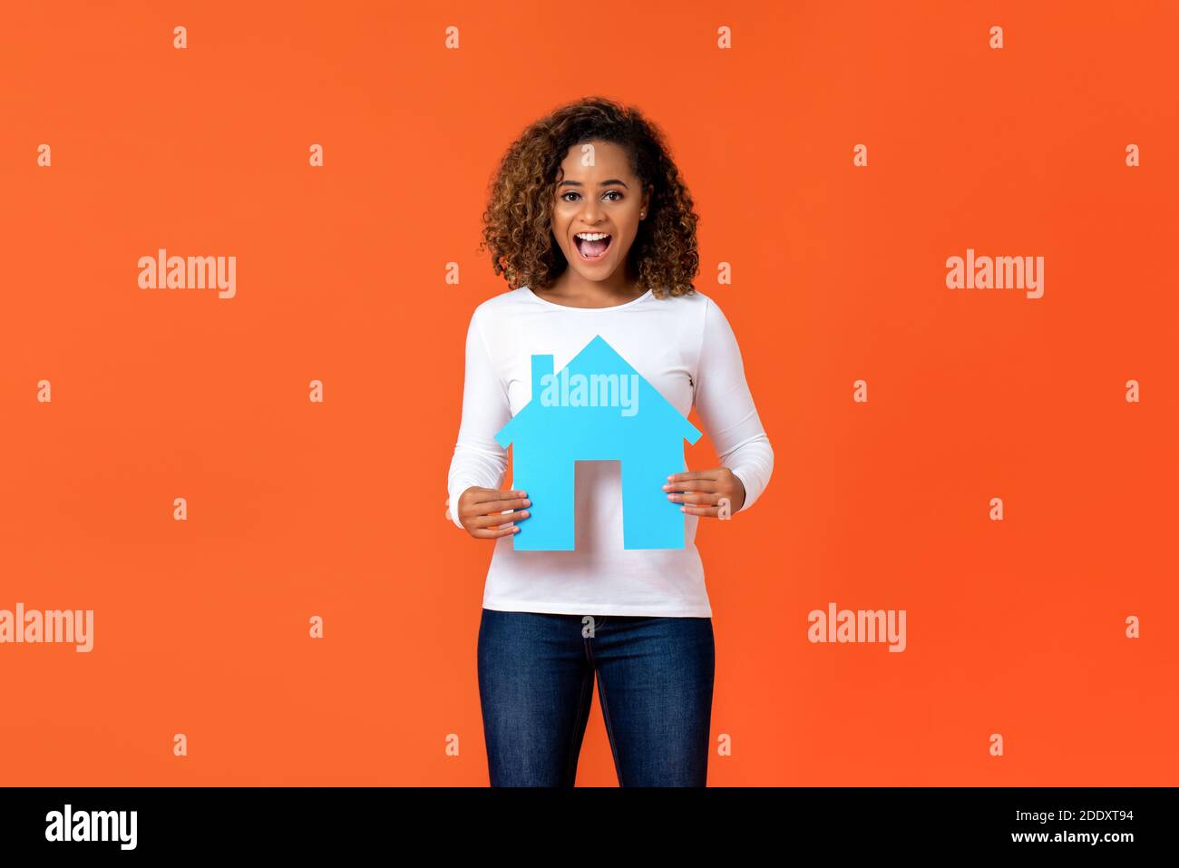 Aufgeregt junge afroamerikanische Frau hält Haus Modell isoliert auf Orange Hintergrund für Immobilien-Konzept Stockfoto