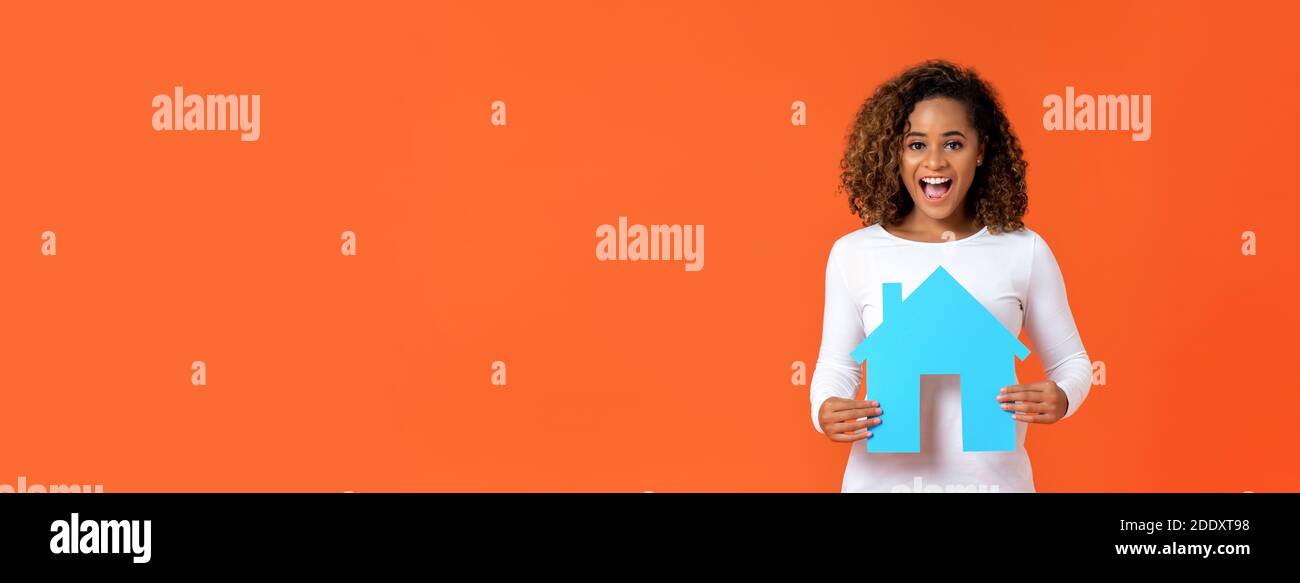 Aufgeregt junge afroamerikanische Frau hält Haus Modell isoliert auf Orange Banner Hintergrund mit Copy Space für Immobilien-Konzept Stockfoto
