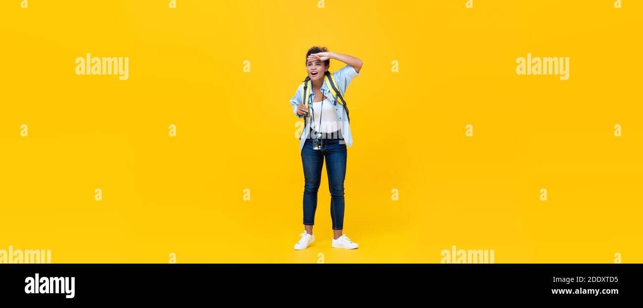 Schöne junge afrikanisch amerikanische Frau Tourist Backpacker Blick weg mit Hand auf Stirn während der Reise isoliert auf gelben Banner Hintergrund Stockfoto
