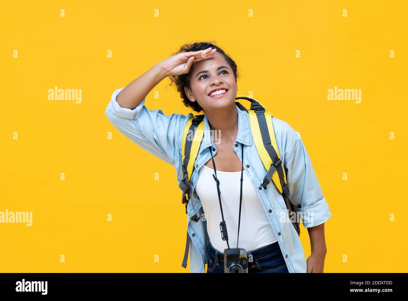 Schöne junge afrikanisch amerikanische Frau Tourist Backpacker Blick weg mit Hand auf Stirn während der Reise isoliert auf gelben Studio Hintergrund Stockfoto