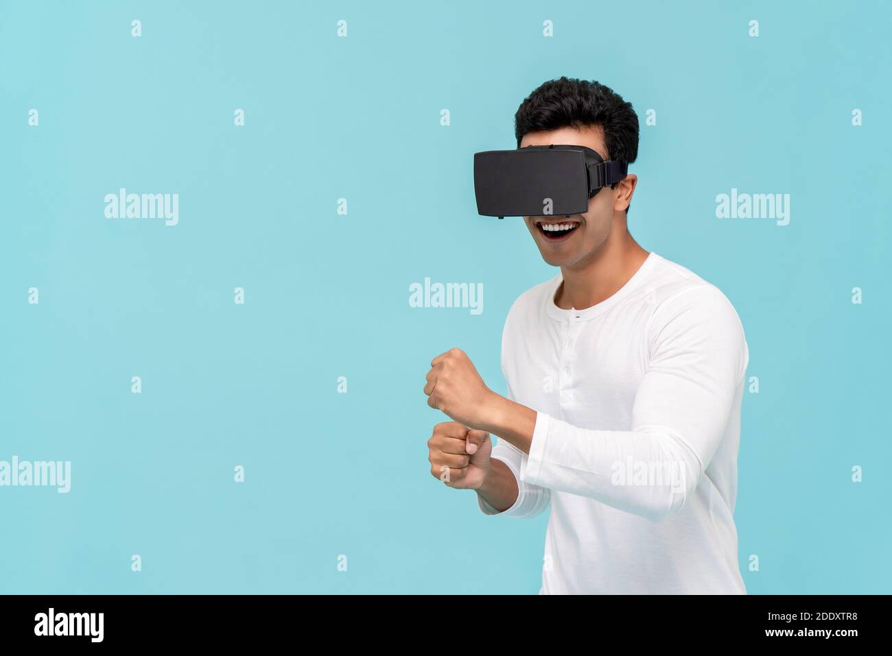 Aufgeregt asiatischen Mann bewegt Körper während der Wiedergabe 3D-Simulation Video Von Virtual Reality oder VR-Brille auf hellblauem Hintergrund Mit Kopierbereich Stockfoto