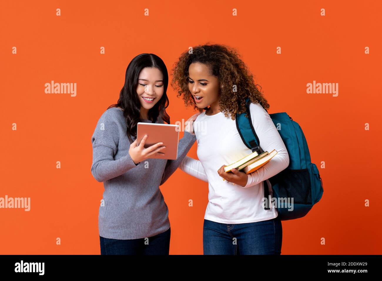 Interracial Studenten als Freunde Blick auf Tablet-Computer isoliert Auf farbenvollem orangefarbenem Hintergrund Stockfoto