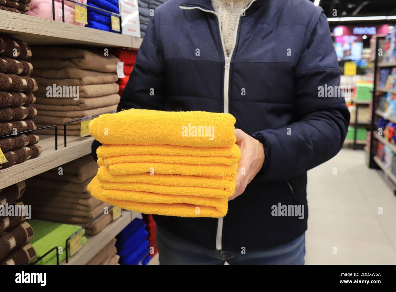 Ein Mann hält einen Stapel Handtücher in einem Geschäft. Hygieneartikel, weiche flauschige gelbe Badetücher im Supermarkt Stockfoto
