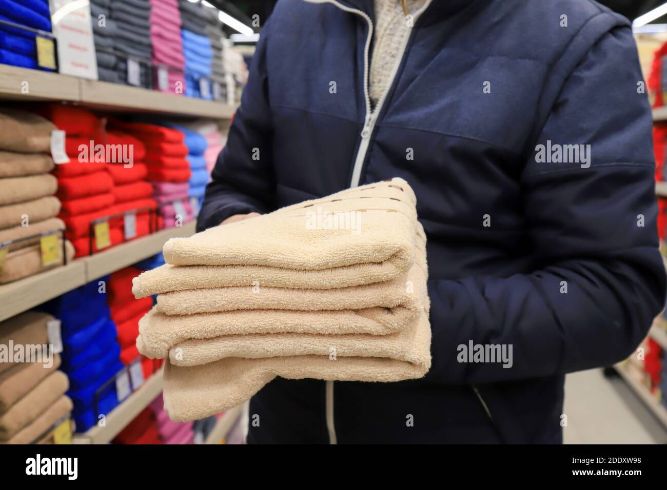 Ein Mann hält einen Stapel Handtücher in einem Geschäft. Hygieneartikel, weiche, flauschige beige Badetücher im Supermarkt Stockfoto
