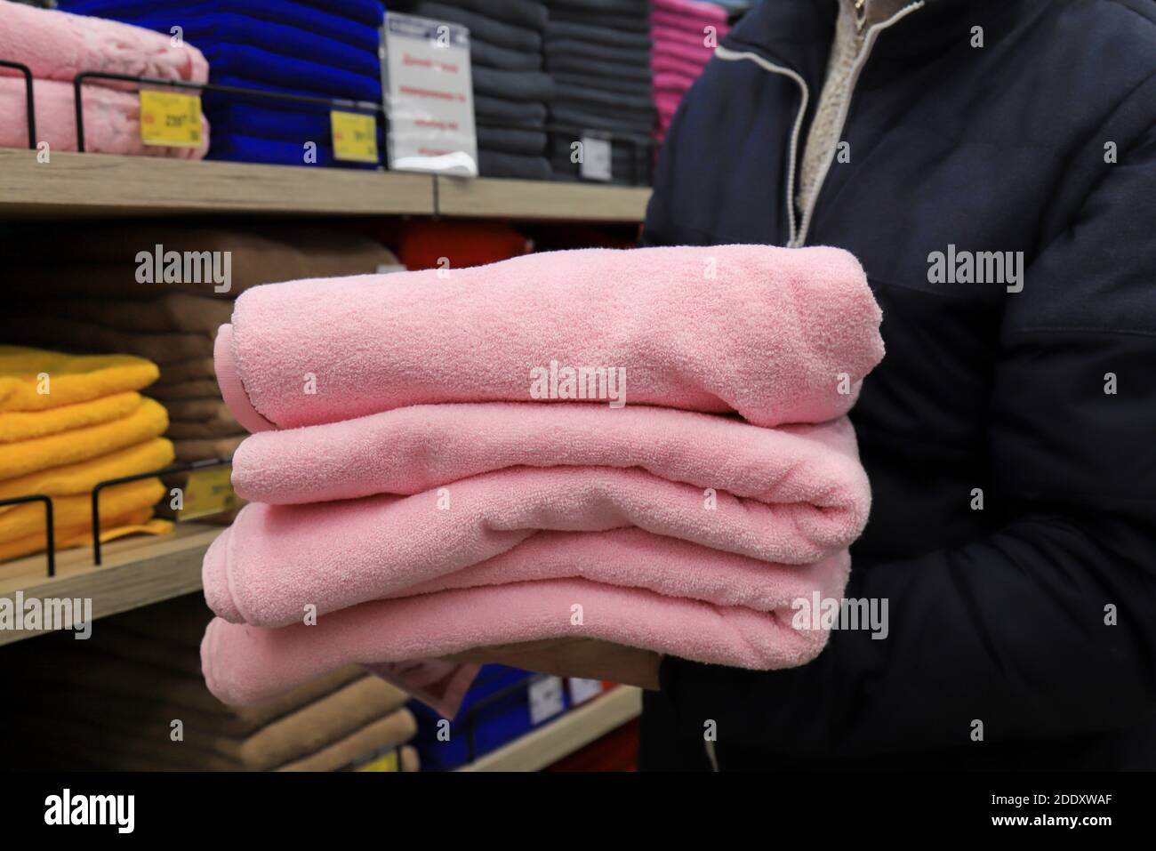 Ein Mann hält einen Stapel Handtücher in einem Geschäft. Hygieneartikel, weiche flauschige rosa Badetücher im Supermarkt Stockfoto