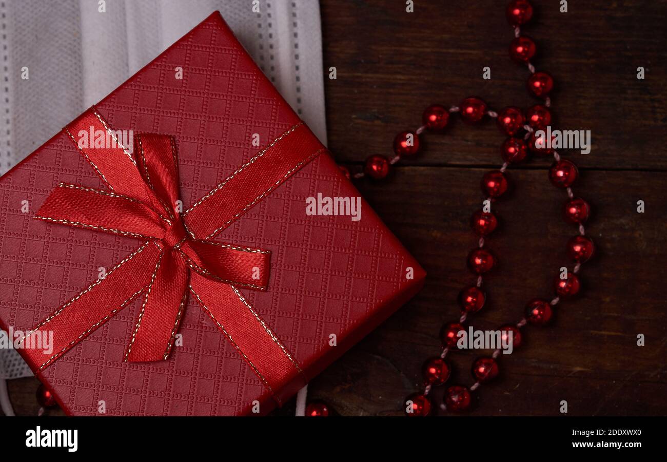 Schutzmaske, rote Geschenkbox und rote Perlen auf braunem Holzhintergrund Stockfoto