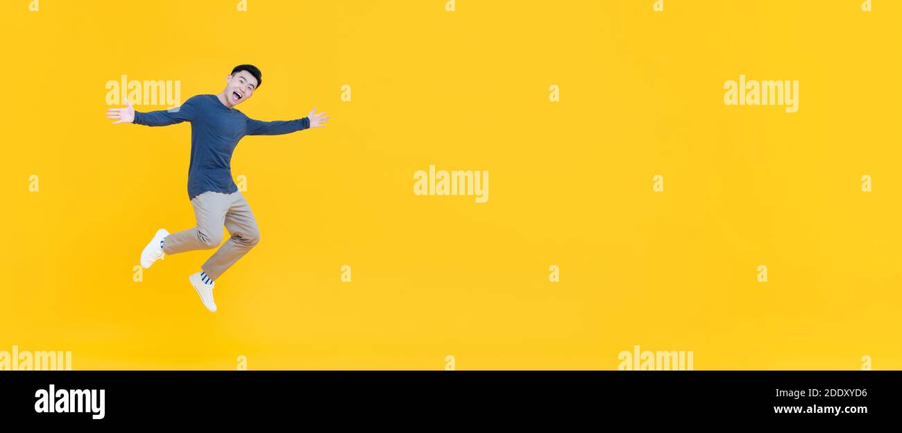 Ganzer Körper der jungen dynamischen schönen asiatischen Mann lächelnd und Springen mit ausgestreckten Armen isoliert auf gelbem Banner Hintergrund mit Speicherplatz kopieren Stockfoto