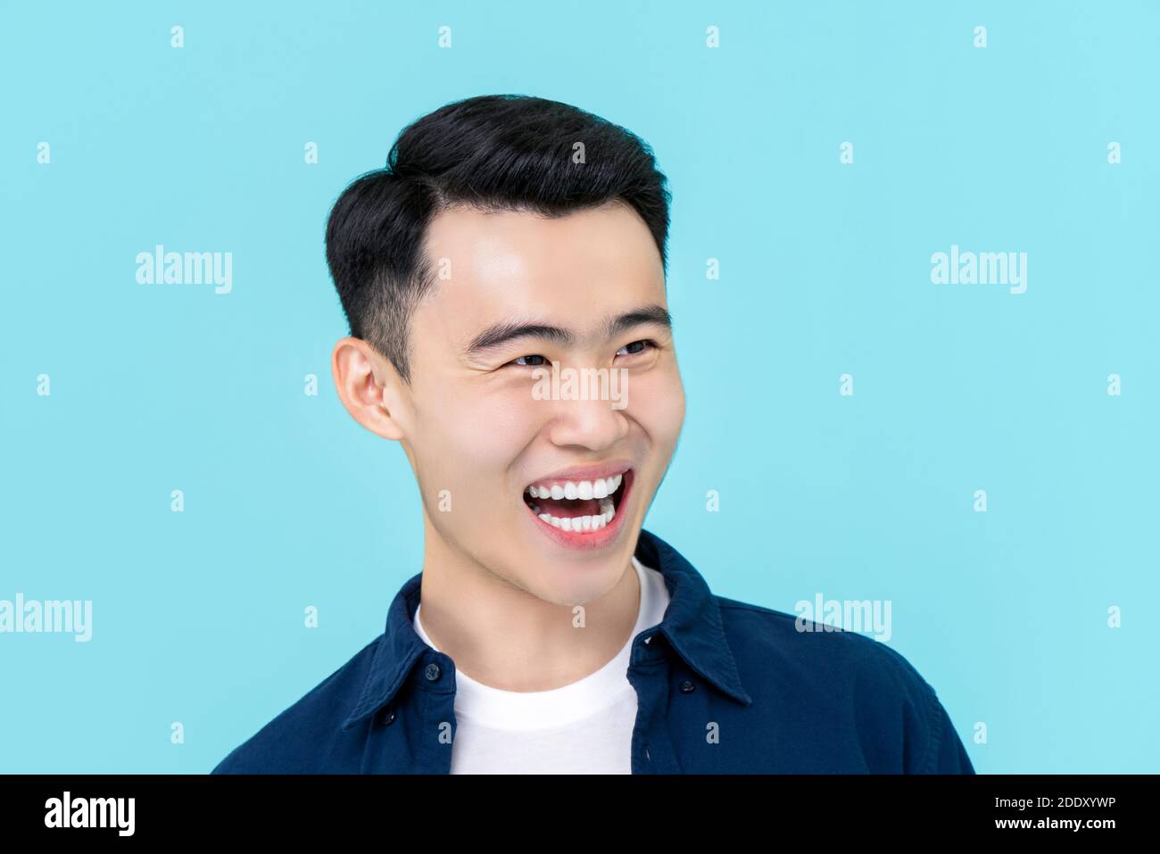 Halbkörper Porträt von jungen asiatischen Mann in schlichten casual Kleidung lachend und lächelnd auf hellblauem Studiohintergrund Stockfoto