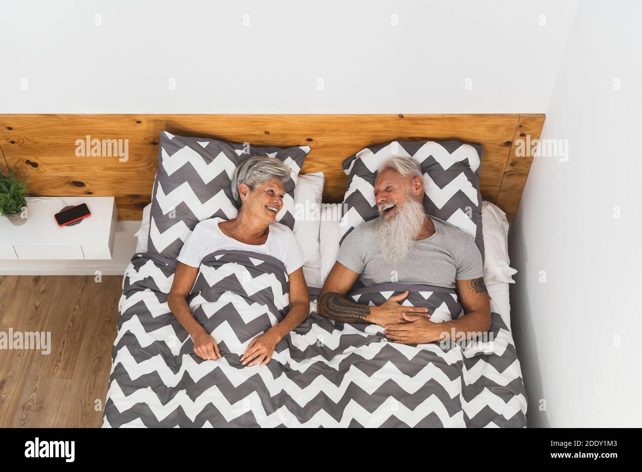 Glückliches Seniorenpaar lächelt zusammen im Bett - Hipster reif Leute, die eine lustige Schlafzeit haben - älterer Lebensstil und Liebe Beziehungskonzept Stockfoto