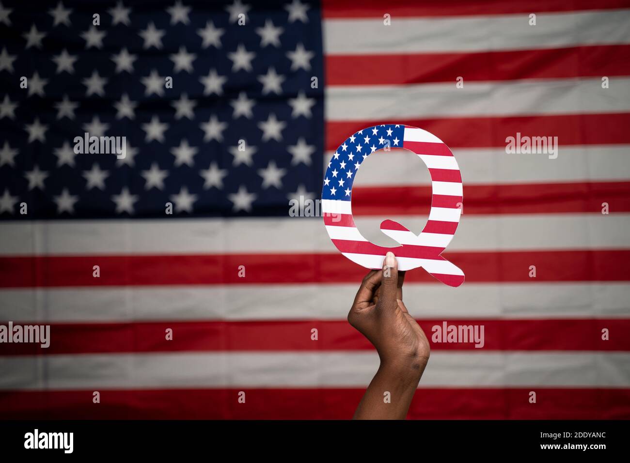 Hände mit Q-Alphabet mit US-Flagge als Hintergrund mit Copy Space - Konzept QAnon oder Q Anon tiefen Zustand Verschwörungstheorie Stockfoto