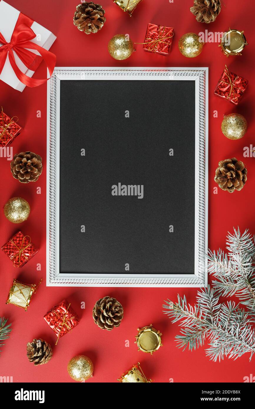 Neujahrsrahmen mit Neujahrsspielzeug, Tannenzweigen und Geschenken in einer Umgebung auf rotem Hintergrund. Grußkarte mit Weihnachten, Neujahr mit gratis Stockfoto