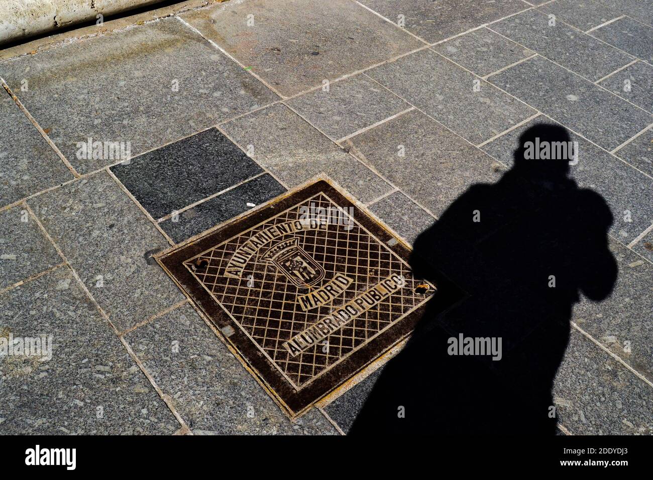 Spanien, Madrid, 17.02.2012. Mannloch in madrid Straße in der Nähe des königlichen Palastes und Schatten des Fotografen. Stockfoto