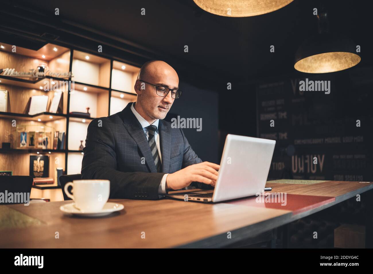 Ein Geschäftsmann mittleren Alters in einer Business-Suite und eine Brille, die spät in einem modernen Büro mit einem Laptop arbeitet. Ein müder Geschäftsmann, der bis spät in die Nacht arbeitet Stockfoto