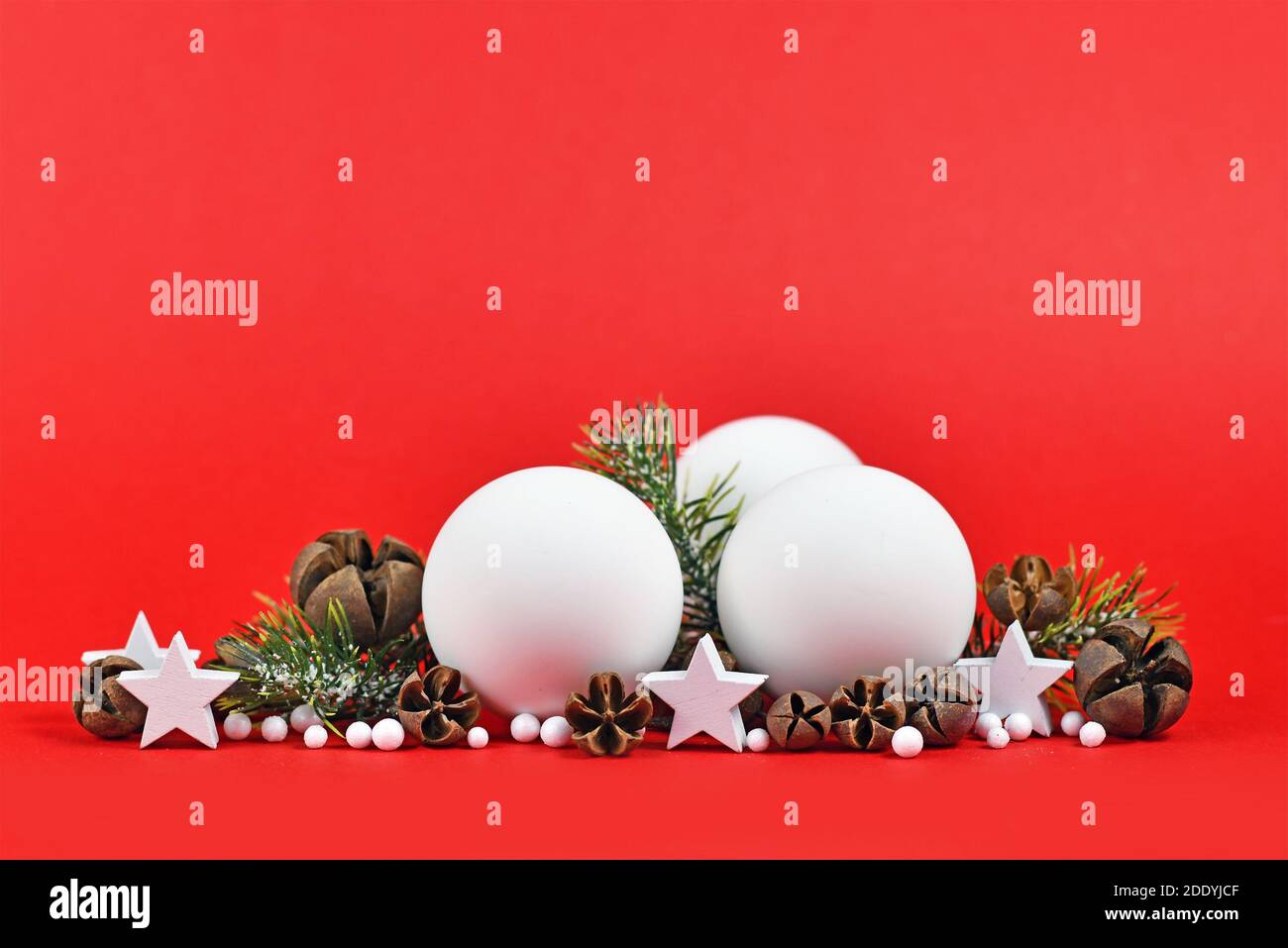 Weihnachtliche Anordnung mit weißen Baumkugeln, Tannenzweigen, Stern- und Schneeballornamenten auf rotem Hintergrund mit Kopierraum Stockfoto