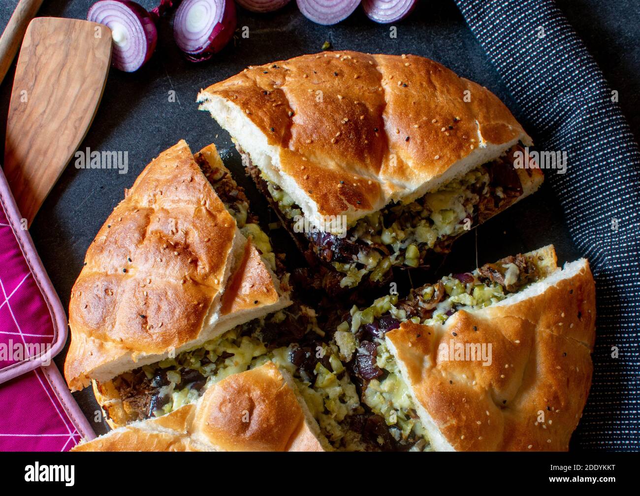 Gefülltes Fladenbrot mit Roastbeef, Käse, Gurken, karamellisierten roten Zwiebeln und Zwiebelsauce serviert auf dunklem Tischhintergrund von oben Stockfoto