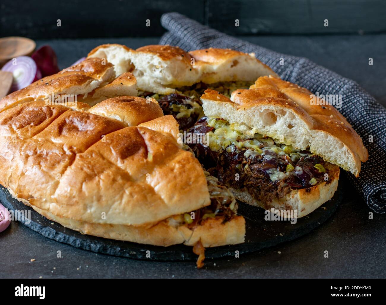 Delilicous Party Snack mit gefülltem amerikanischen Fladenbrot mit langsam gekochtem gebratenem Rindfleisch, karamellisierten Zwiebeln, Käse und Gurken auf dunklem Teller serviert Stockfoto