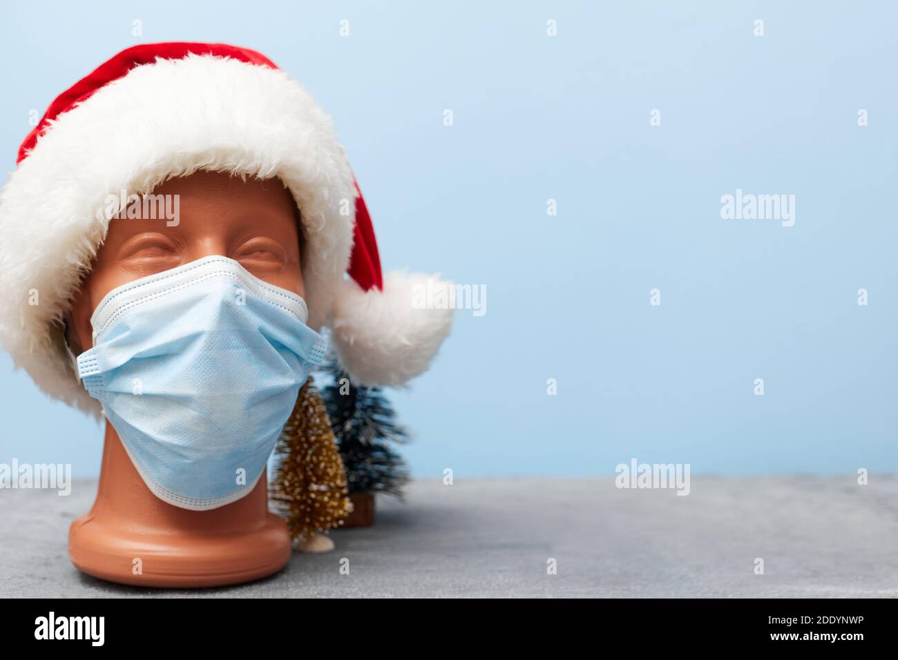 Covid 19, medizinische Maske auf einer Schaufensterpuppe und weihnachtshut 2021 auf blauem Hintergrund, Banner, Kopierraum Stockfoto