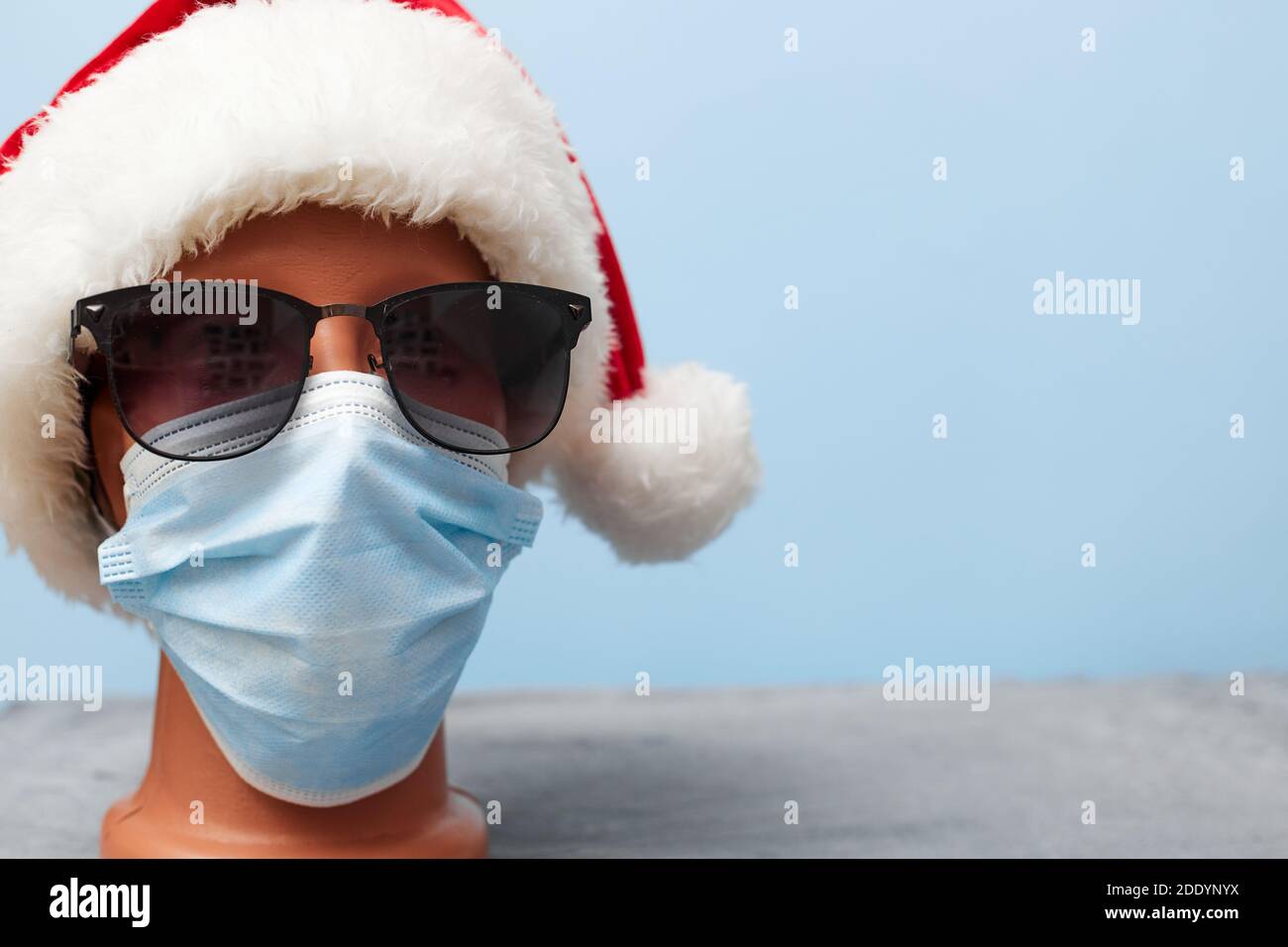 Medizinische Maske auf einer Schaufensterpuppe und ein Neujahr Hut weihnachten 2021 auf einem blauen Hintergrund, Banner, Kopierraum Stockfoto