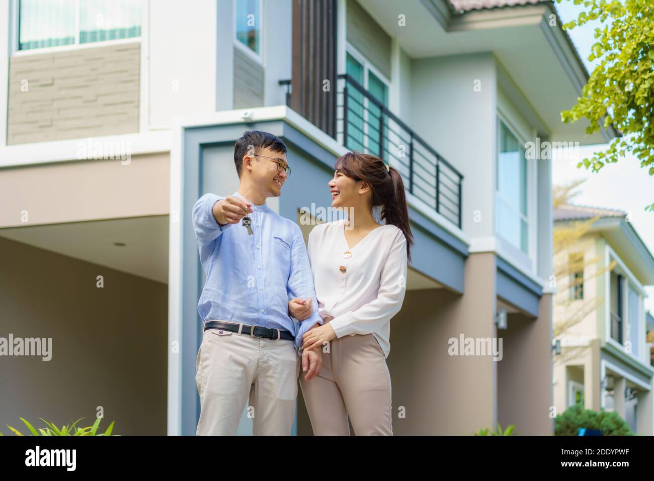 Porträt des jungen asiatischen Paares, das zusammen steht und umarmt und die Haustaste hält, die vor ihrem neuen Haus glücklich aussieht, um neues Leben zu beginnen. Familie Stockfoto