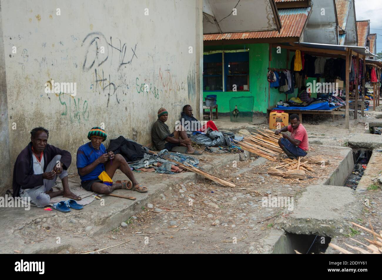 Marktszene eines großen Marktes am Stadtrand von Wamena, West Papua, Indonesien. Männer, die gegen die Wand sitzen und auf einen Job warten. Stockfoto