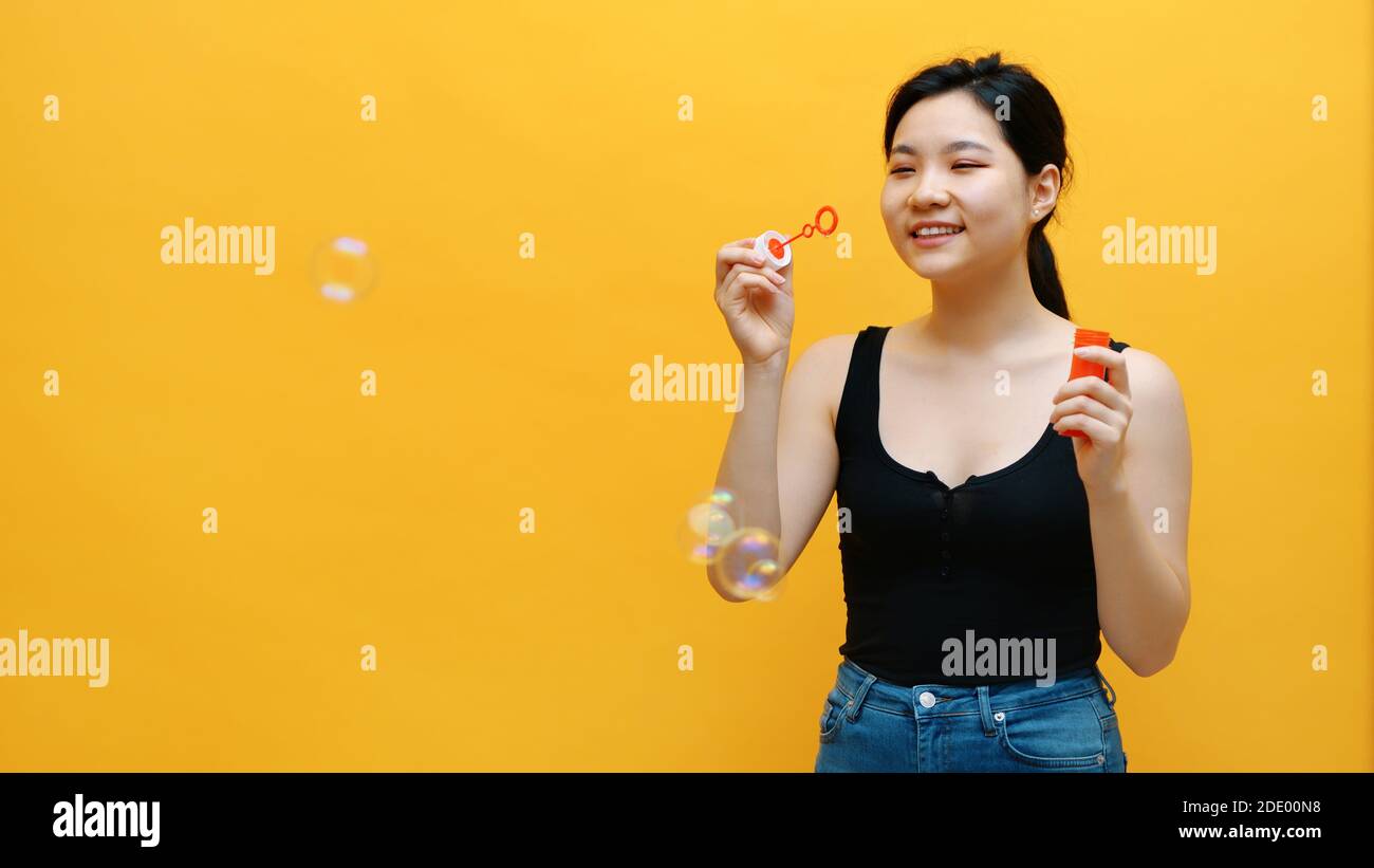 Kindisch junge asiatische Frau Seifenblasen. Isoliert auf gelbem Hintergrund. Hochwertige Fotos Stockfoto