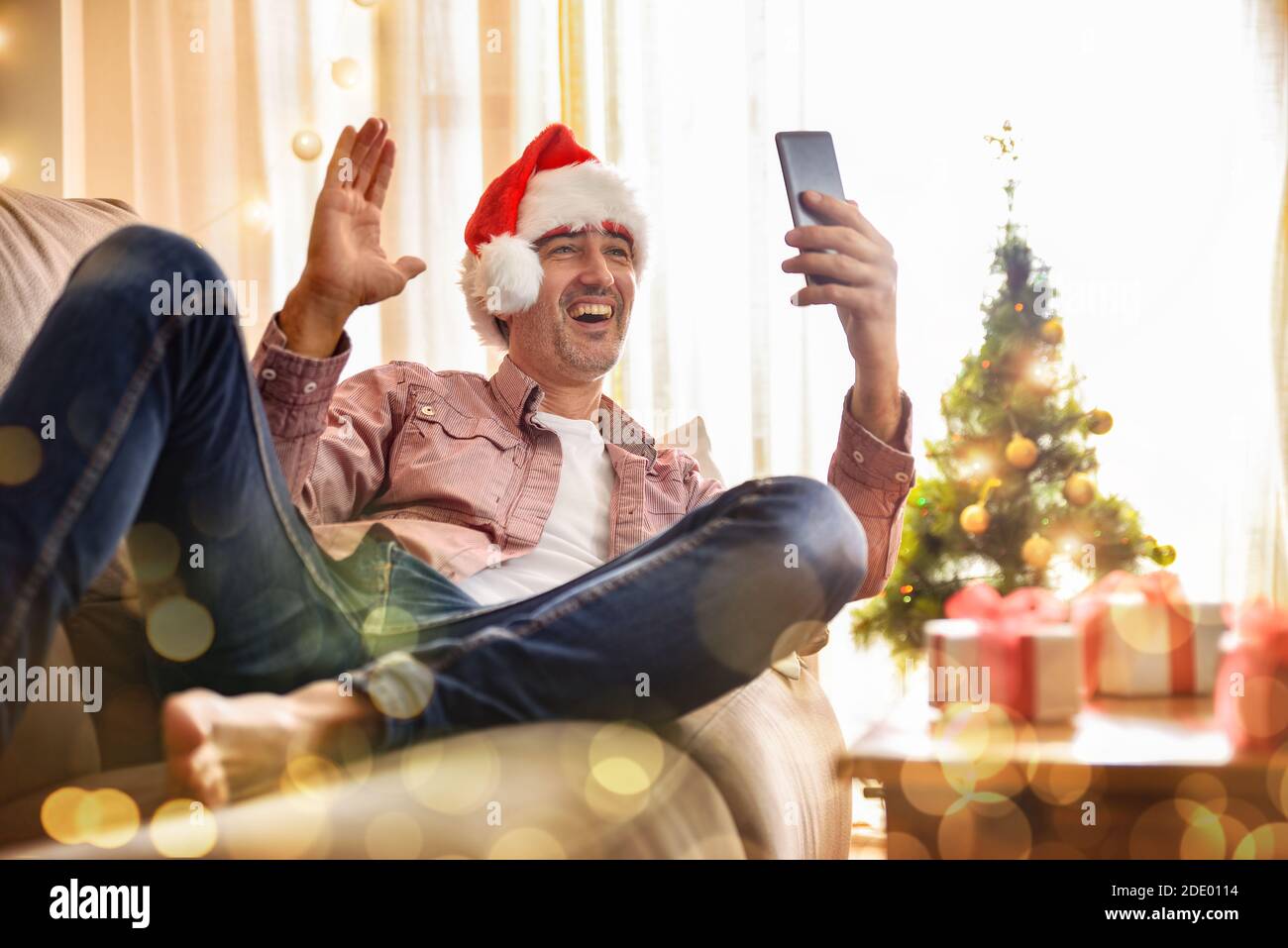 Mann mit Weihnachtshut auf einem Sofa liegend gratuliert Ein Videoanruf von einem Mobiltelefon von zu Hause aus Stockfoto