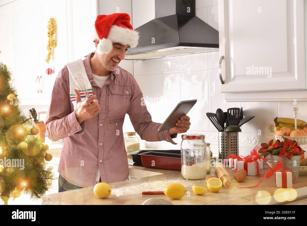 Mann kocht Desserts zu Hause Beratung Rezepte auf einem Tablet an weihnachten. Horizontale Zusammensetzung. Stockfoto