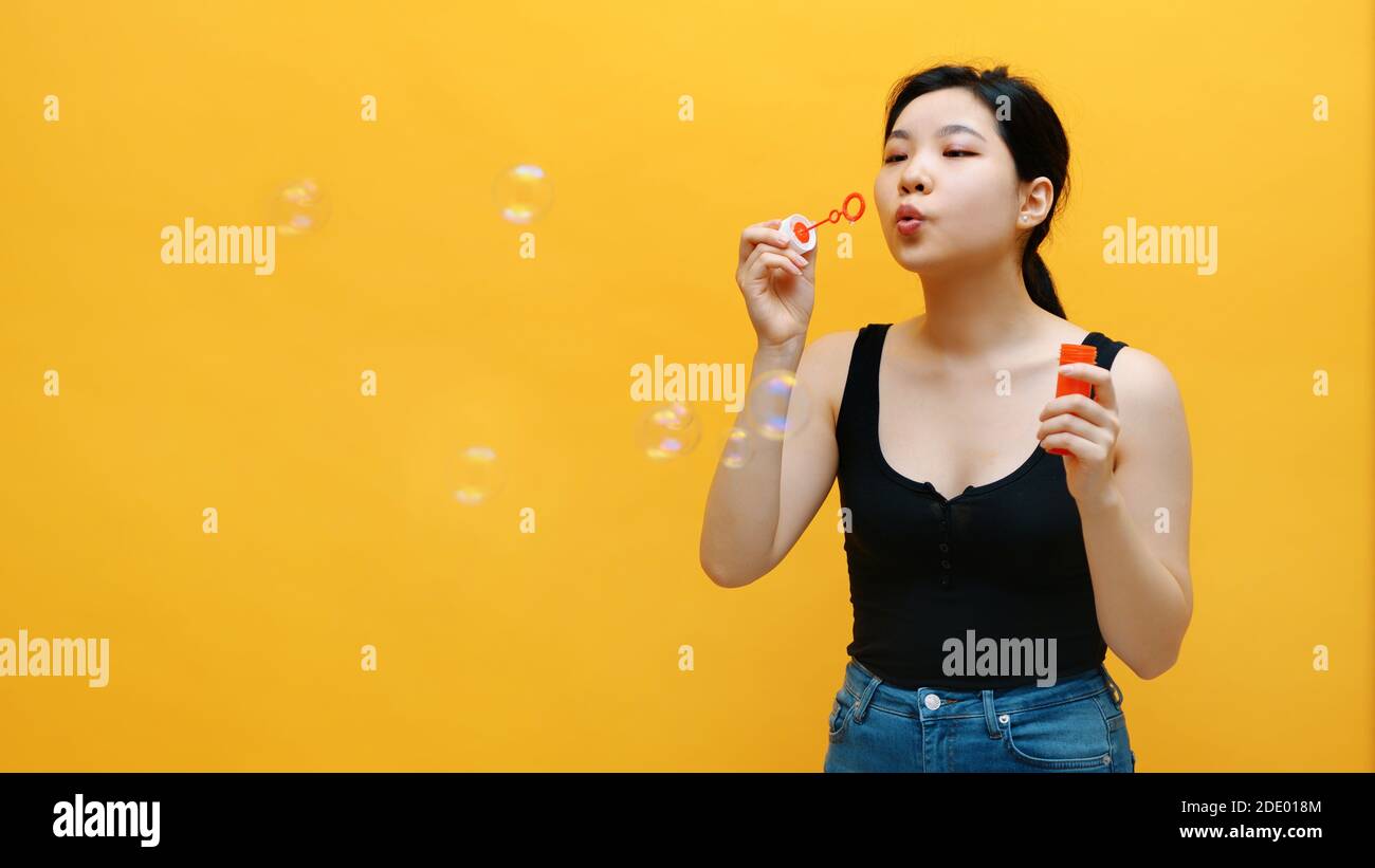 Glücklich junge asiatische Frau Seifenblasen. Isoliert auf gelbem Hintergrund. Hochwertige Fotos Stockfoto