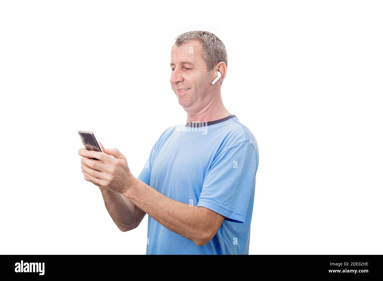 Lächelnder Mann mittleren Alters mit Smartphone und SMS, während Musik mit einem Ohrstöpsel hören. Stockfoto