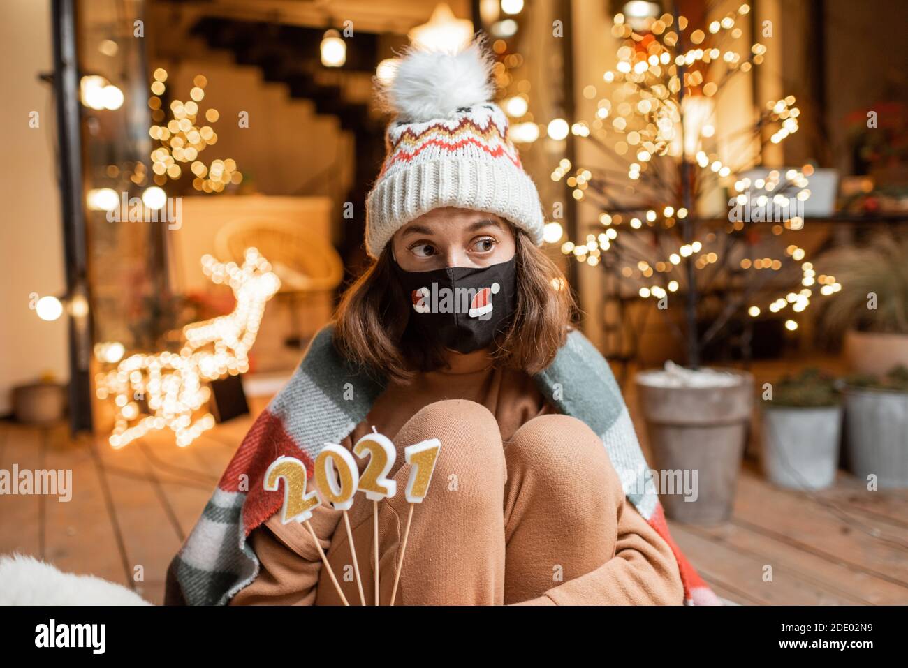 Porträt einer traurigen Frau in Gesichtsmaske feiern allein Neujahr. Kerzen halten 2021 mit der Hoffnung, dass die Quarantäne endet Stockfoto