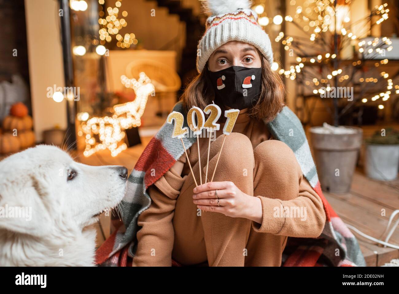 Porträt einer traurigen Frau in Gesichtsmaske feiern allein Neujahr. Kerzen halten 2021 mit der Hoffnung, dass die Quarantäne endet Stockfoto
